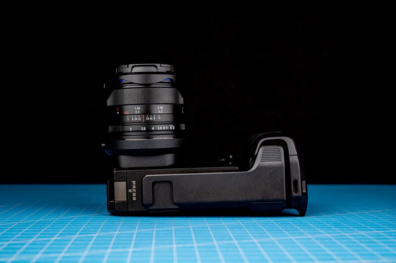 A black camera body with a lens attached is resting on its side on a blue grid mat against a black background.