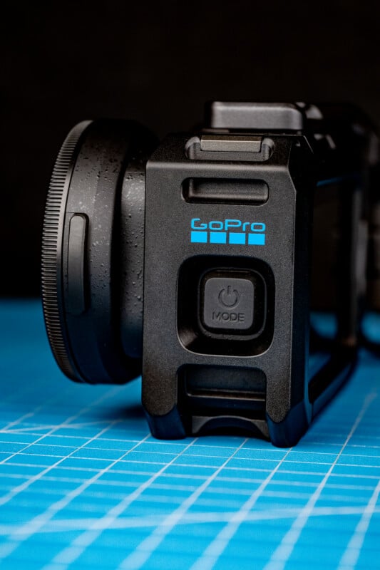 A black GoPro camera housing with a power button sits on a blue grid cutting mat against a dark background.