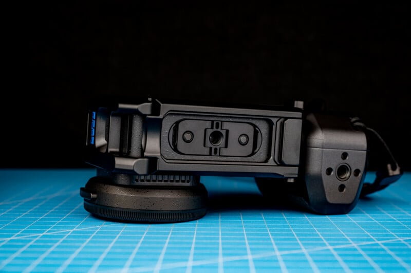 A black camera accessory with a lens cap rests on a blue grid cutting mat against a black background.