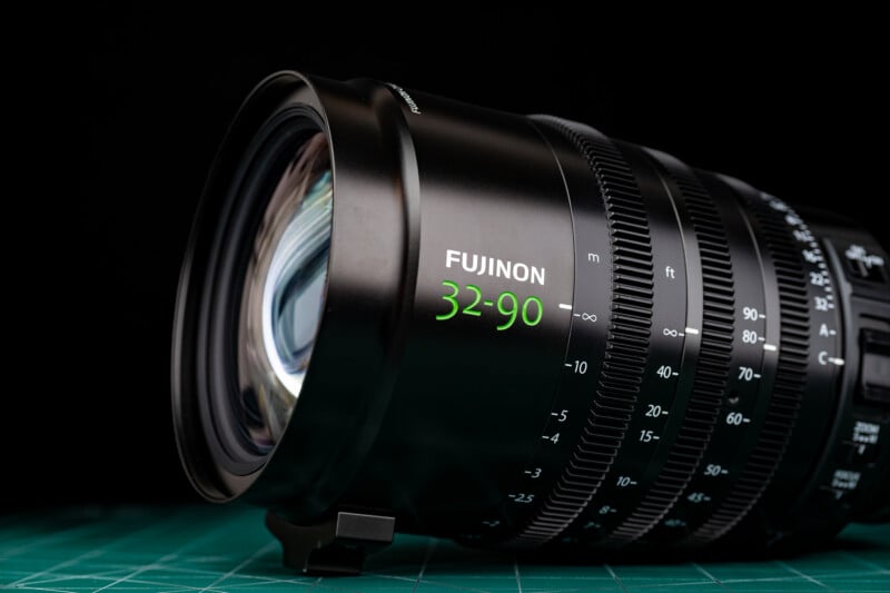 A black Fujinon 32-90 cinema zoom lens sits on a green cutting mat against a black background.