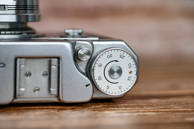 A close-up view of the top plate of a vintage silver film camera, showing a circular frame counter dial set near zero and a metal accessory shoe.