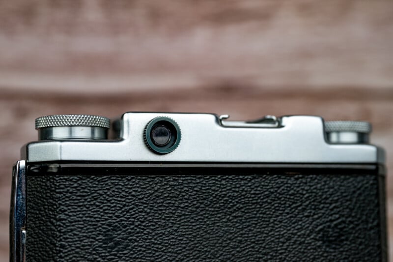 A close-up view of the top section of a vintage film camera, showing the viewfinder, a circular dial, and textured black leatherette casing.