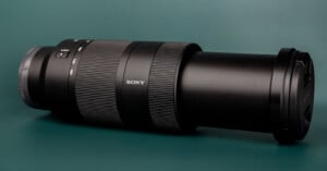 A black Sony telephoto zoom lens with a lens cap attached, resting horizontally on a dark green surface.