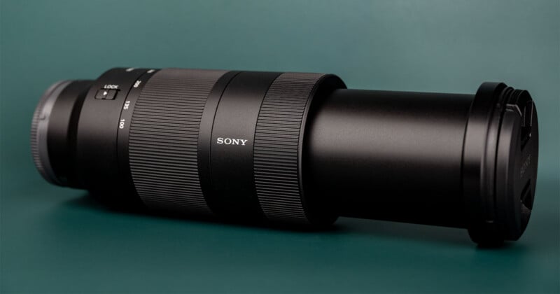 A black Sony telephoto zoom lens with a lens cap attached, resting horizontally on a dark green surface.