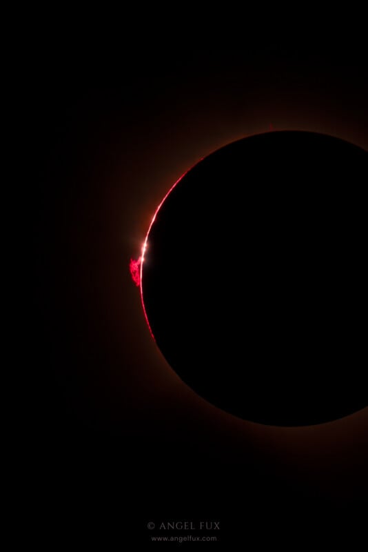 A total solar eclipse shows a dark lunar silhouette surrounded by a thin, glowing red ring of the sun's chromosphere and a prominence.