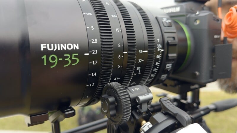 A close-up view of a Fujinon 19-35 lens attached to a camera, featuring a focus gear ring with distance markings and a SmallRig follow focus unit mounted below.
