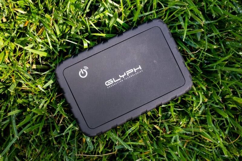 A black Glyph Production Technologies external hard drive rests on a patch of green grass.
