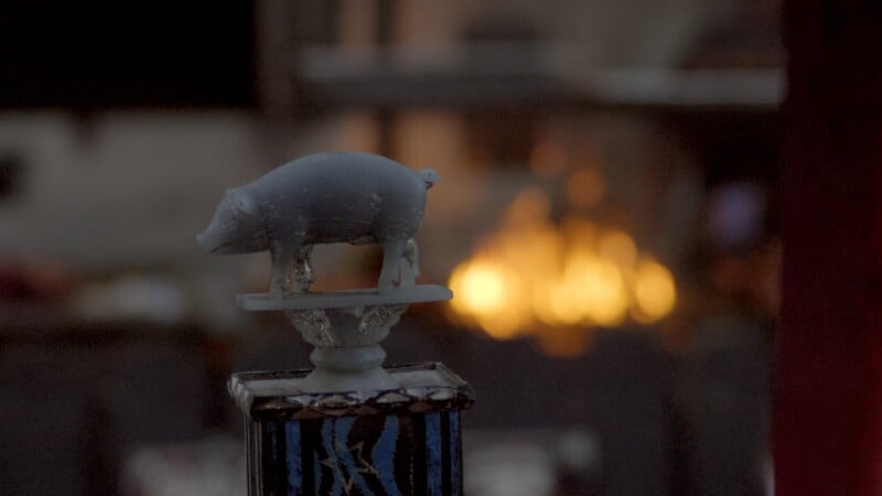 A small, light-colored pig figurine stands on a pedestal against a blurred, glowing orange background.