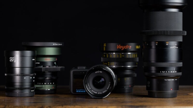 A collection of various camera lenses and a GoPro camera arranged on a wooden surface against a black background.