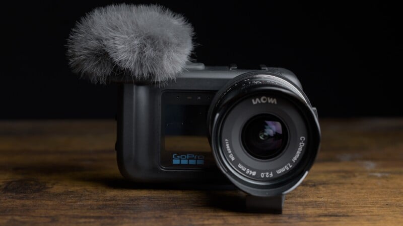 A GoPro camera with a Laowa C-Dreamer 7.5mm lens and a fuzzy microphone windscreen sits on a wooden surface against a black background.
