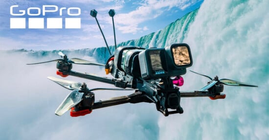 A GoPro-branded FPV drone with a mounted camera flies in front of a large waterfall.
