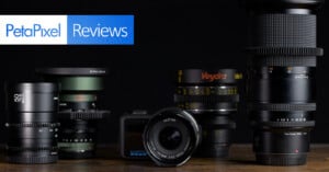 A collection of various camera lenses and a GoPro camera sit on a wooden surface against a black background, with a PetaPixel Reviews logo in the top left corner.