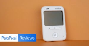 A white Godox device with a screen and control buttons sits against a solid orange background, with a PetaPixel Reviews logo in the corner.