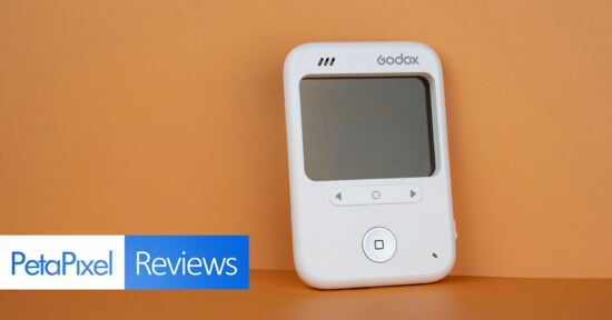 A white Godox device with a screen and control buttons sits against a solid orange background, with a PetaPixel Reviews logo in the corner.