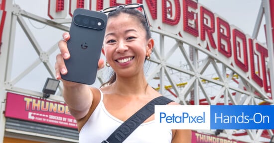 A smiling woman holds a dark smartphone toward the camera in front of a large sign that reads "THUNDERBOLT.