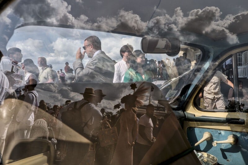 A double exposure photograph shows a crowd of people outdoors overlaid with the interior of a vintage car, including its window frame and door handle.