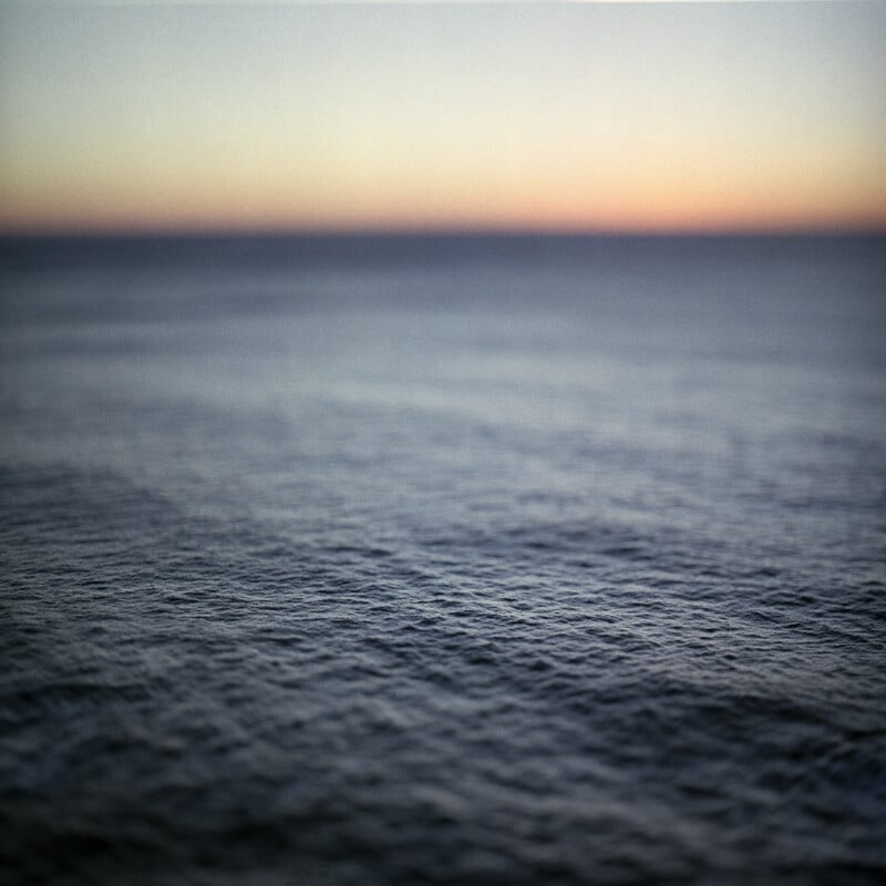 A close-up view of dark, rippling ocean water transitions into a soft, hazy horizon at sunset.
