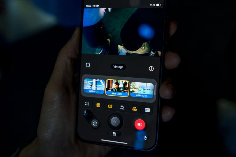 A hand holds a smartphone displaying a camera app interface with a live video feed, filter selection options, and a red record button.