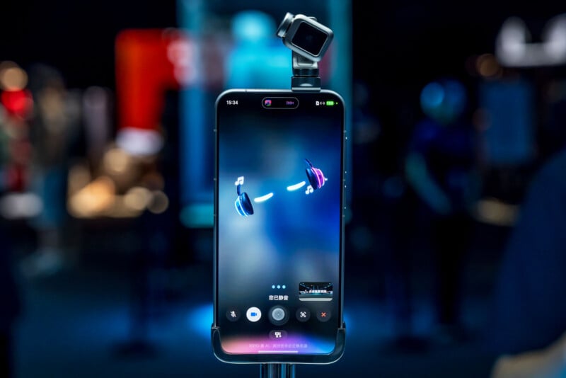 A smartphone mounted on a stand with a small external camera attached to its top, displaying a digital interface with headphone icons and Chinese text on a dark background.