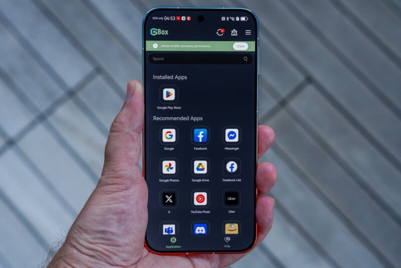 A hand holds a smartphone displaying the GBox app interface, which lists installed and recommended applications.