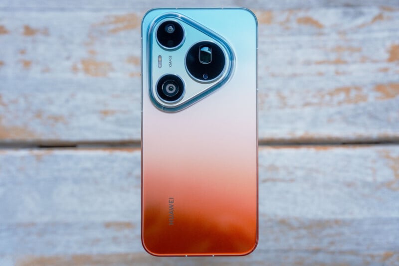 A smartphone with a gradient blue-to-orange back panel and a triangular camera module sits on a weathered white wooden surface.
