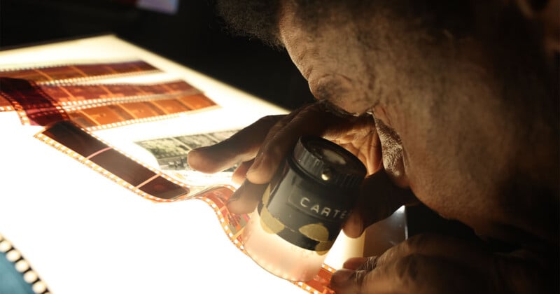 A person uses a magnifying loupe to examine a strip of photographic film on a light table.