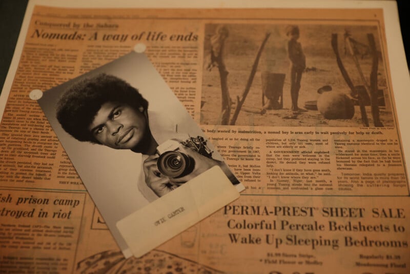 A black-and-white portrait of a man holding a camera is placed over a newspaper page featuring an article about nomadic life.