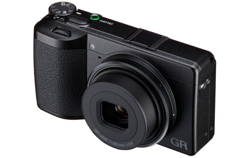 A black Ricoh GR IIIx digital camera angled to show the front and top, featuring a fixed 26.1mm f/2.8 lens and a mode dial.