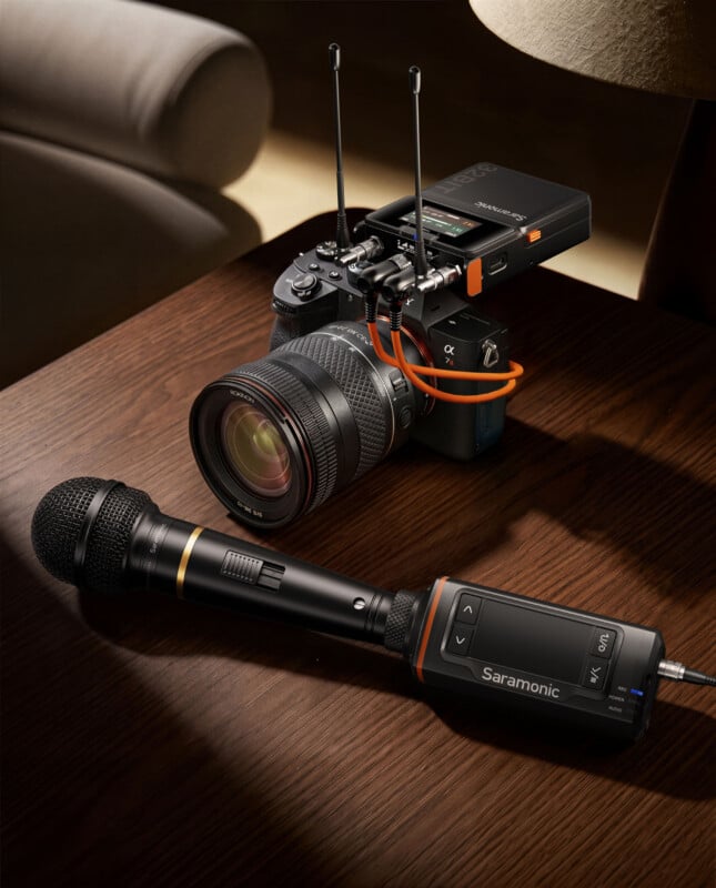 A Saramonic wireless microphone receiver is mounted on top of a camera, with a handheld Saramonic microphone lying on a wooden table in the foreground.