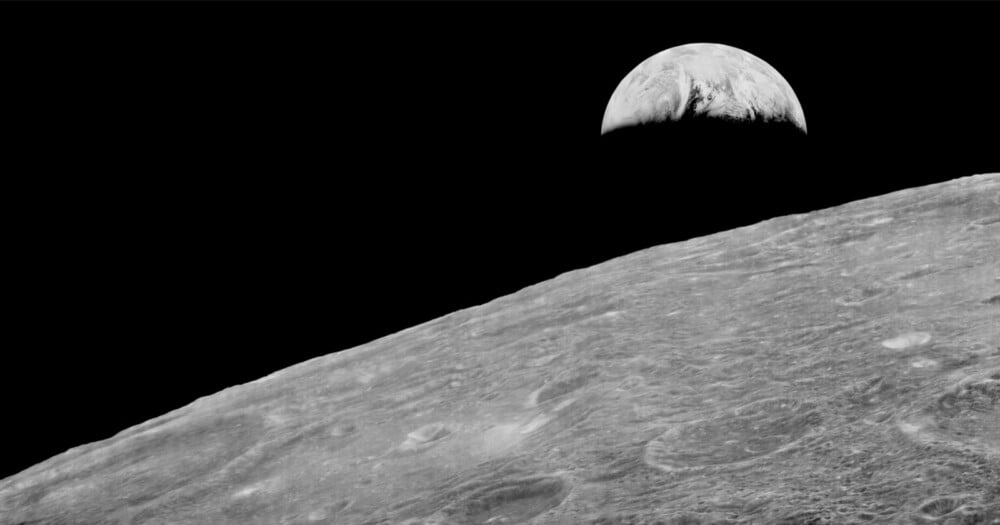 A black-and-white view of the Earth rising above the cratered, barren horizon of the Moon.