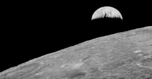 A black-and-white view of the Earth rising above the cratered, barren horizon of the Moon.