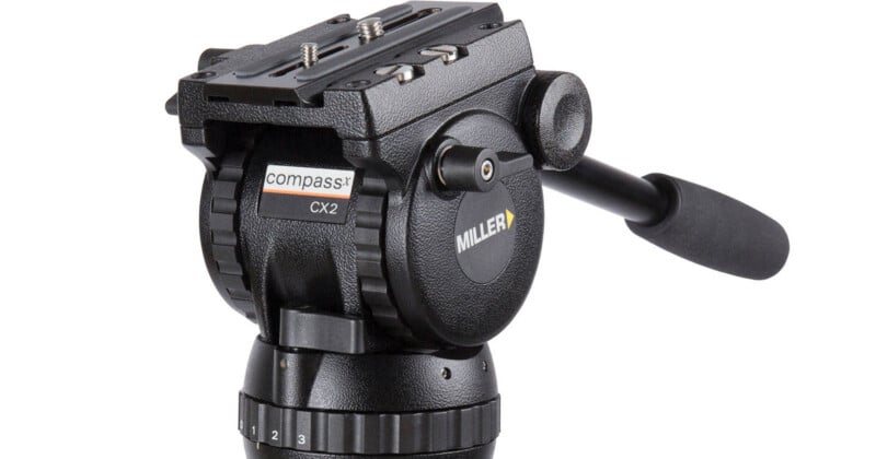 A black Miller Compass CX2 fluid tripod head with a pan handle, mounting plate, and numbered adjustment dials.