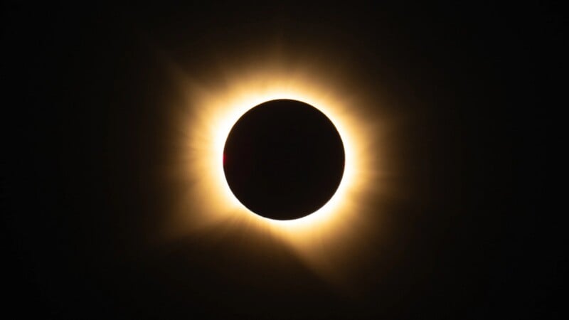 A total solar eclipse showing the dark silhouette of the moon surrounded by a bright, glowing solar corona against a black sky.