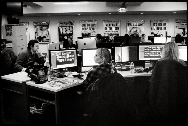 Three people work at computers in an office decorated with framed historic newspaper front pages on the wall.