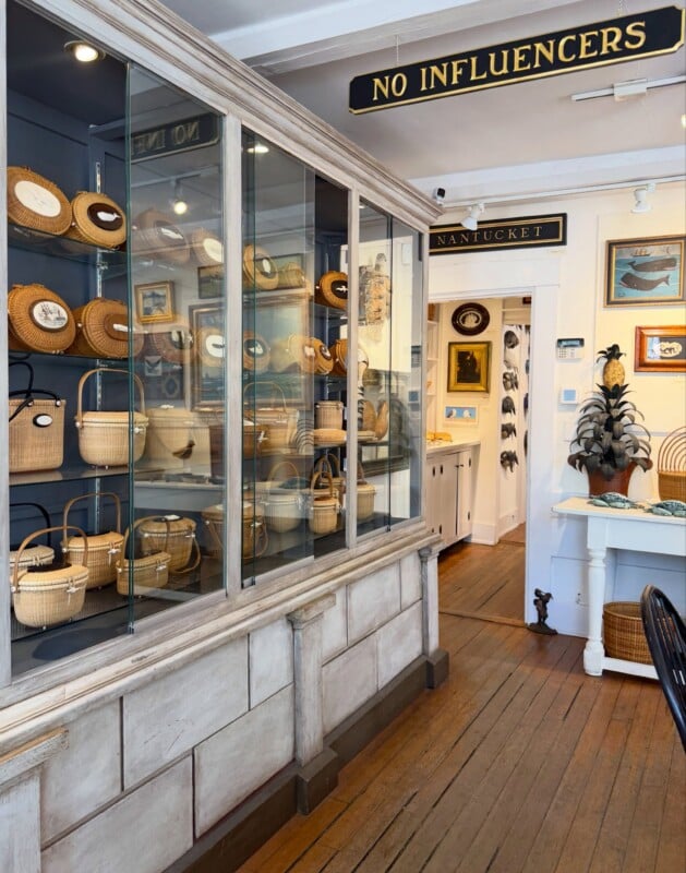 A large glass display case filled with woven Nantucket baskets stands in a shop with a sign that reads "NO INFLUENCERS.