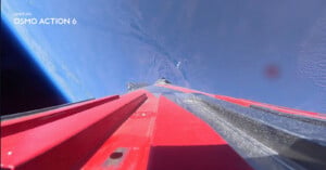 A high-angle view from a camera mounted on a red and black structure, looking down toward the Earth's surface from space.