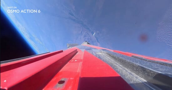 A high-angle view from a camera mounted on a red and black structure, looking down toward the Earth's surface from space.