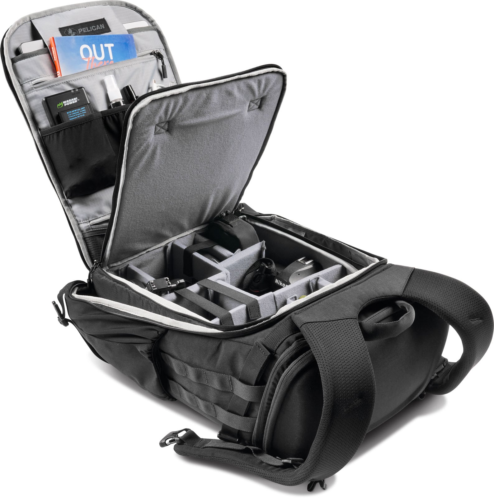 An open black camera backpack lies on its back, revealing interior padded dividers, accessory pockets, and a book labeled "OUT".