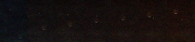 A series of eight faint, glowing circular objects are arranged in a horizontal line against a dark, grainy background.