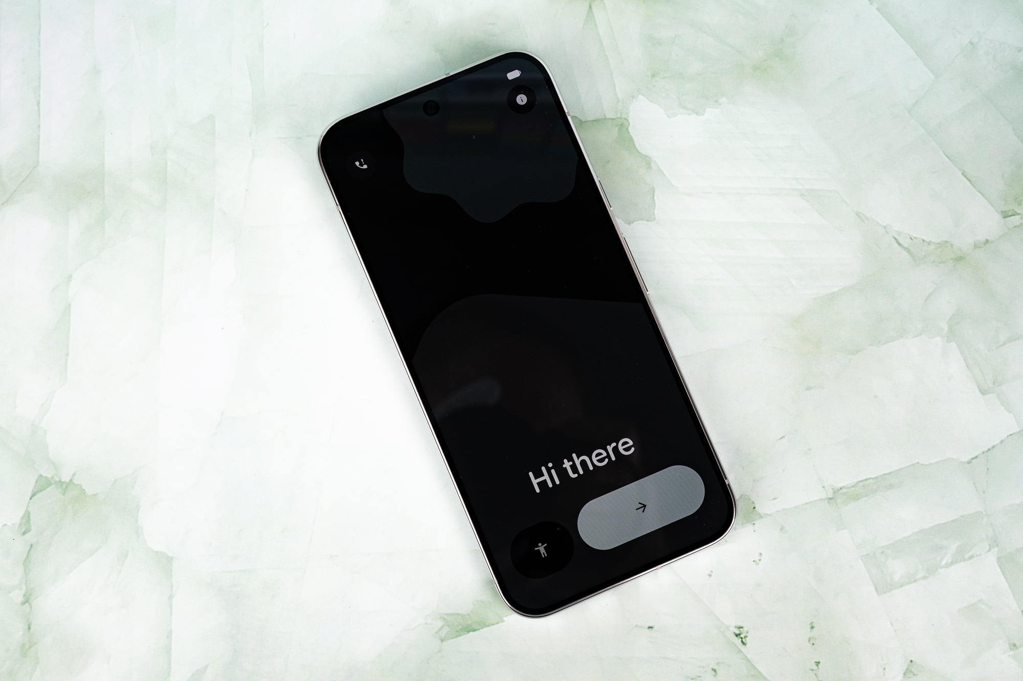 A smartphone screen displays a "Hi there" welcome message on a black background, resting on a light green marble surface.