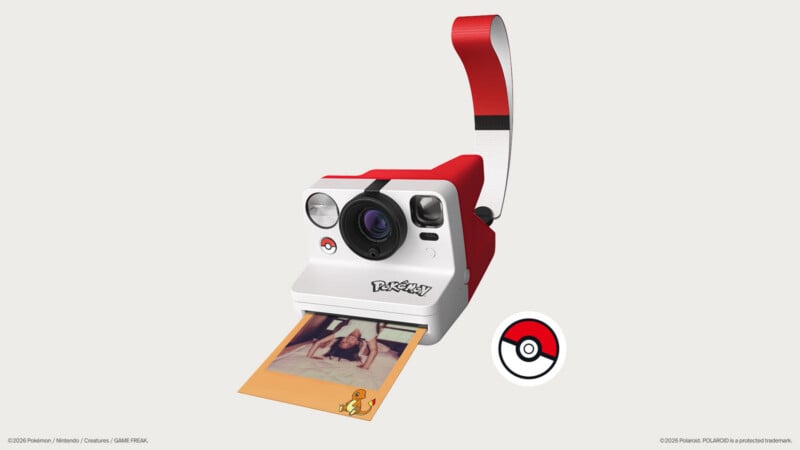 A red and white Pokémon-themed instant camera with a matching strap, ejecting a photo featuring a Charmander graphic, next to a Poké Ball icon.