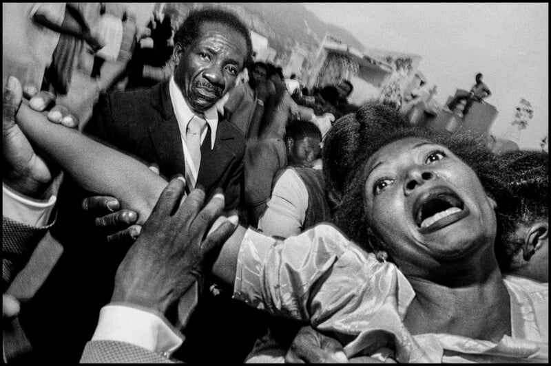 A man in a suit holds the arm of a woman who is looking upward with an expression of distress or intense emotion.