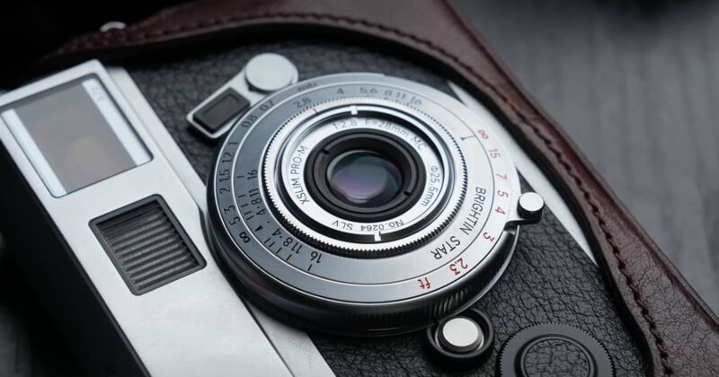 A close-up view of a silver camera lens with a black leather casing, showing focus and aperture markings.