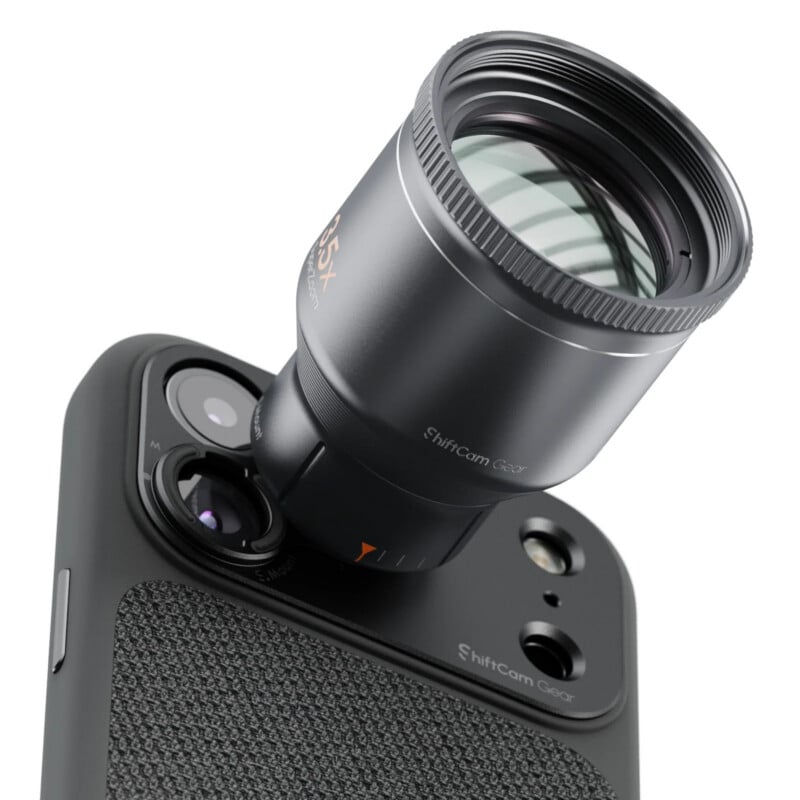 A ShiftCam Gear telephoto lens attachment is mounted onto the camera array of a smartphone in a textured black case.