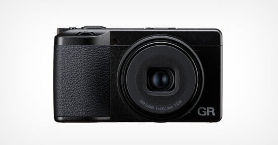 A front-facing view of a black compact digital camera with a textured grip on the left side and a lens labeled "GR LENS f=26.1mm 1:2.8" on the right.