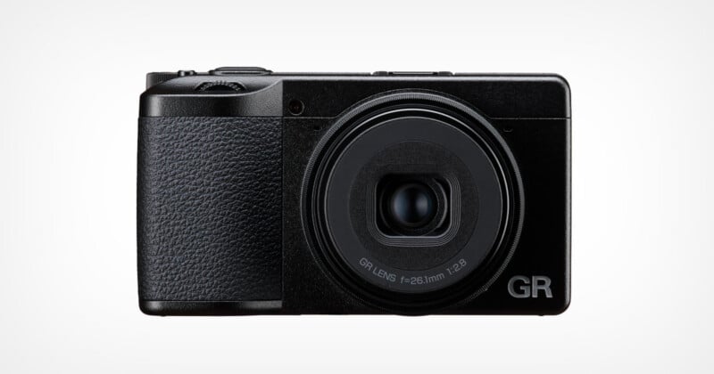 A front-facing view of a black compact digital camera with a textured grip on the left side and a lens labeled "GR LENS f=26.1mm 1:2.8" on the right.