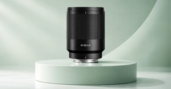 A black camera lens labeled "AF 85/1.8" stands upright on a circular, light green pedestal against a matching curved background.