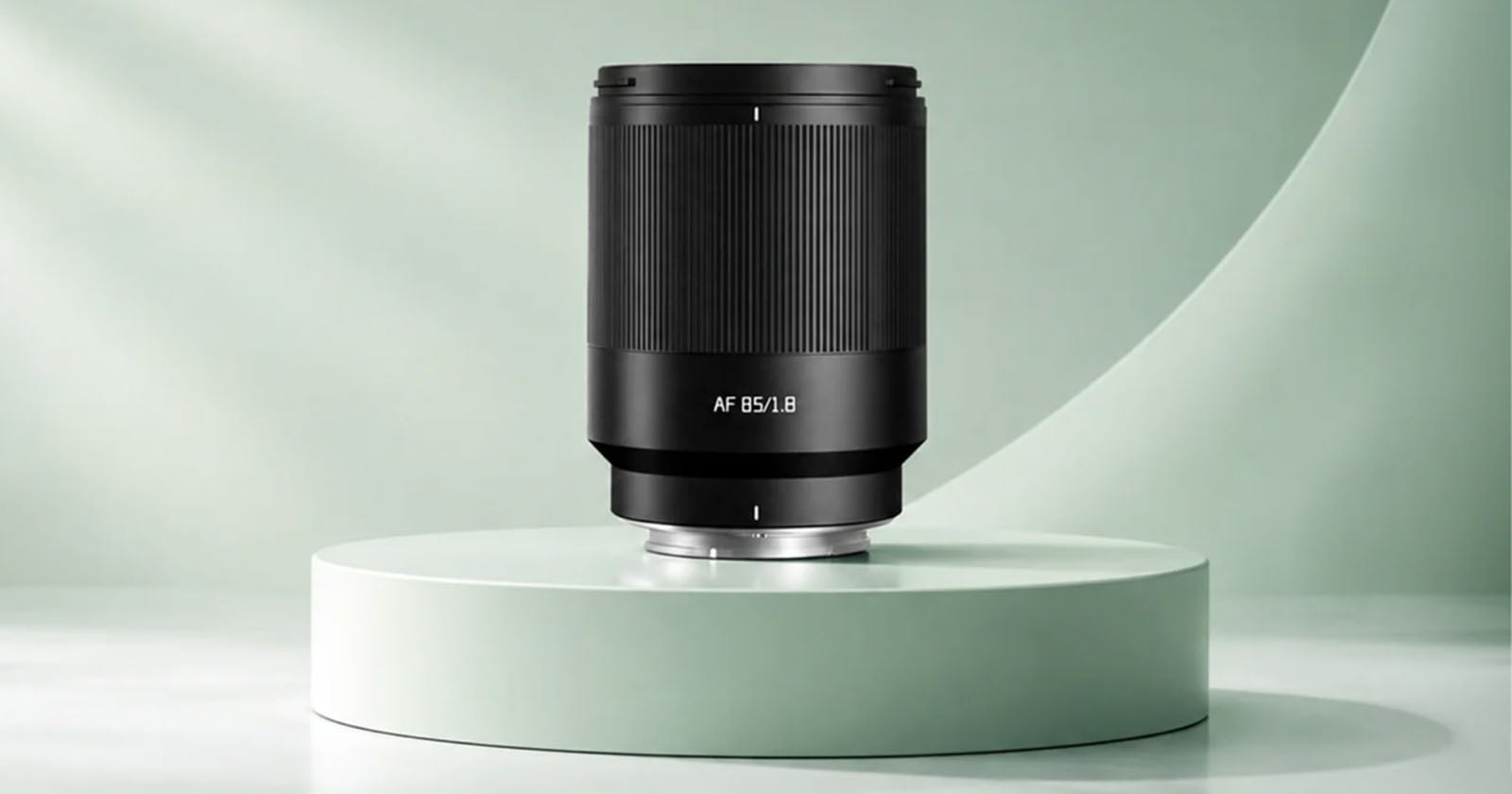 A black camera lens labeled "AF 85/1.8" stands upright on a circular, light green pedestal against a matching curved background.