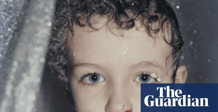 A close-up portrait of a young child with wet hair and skin, with a small cluster of teeth visible near their left eye.