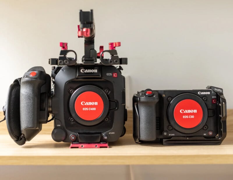 Two Canon cinema cameras, a larger EOS C400 on the left and a smaller EOS C50 on the right, sit side-by-side on a wooden surface.